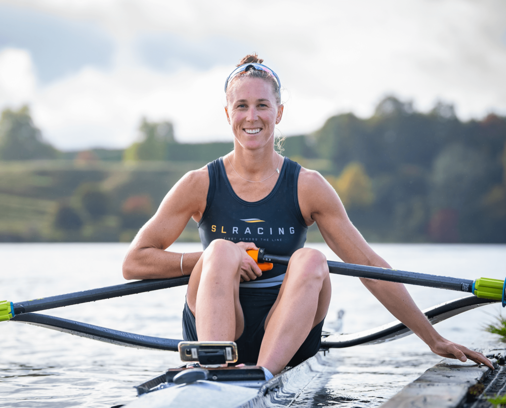 New Zealand Rowing Champion, Emma Twigg, sits in a single SLRacing scull holding onto the pontoon smiling at camera.